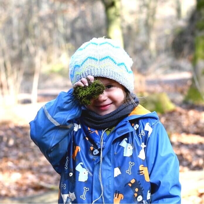 Auf dem Bild zu sehen ist ein Kind der Kita Albach, das Moos in die Kamera hält.