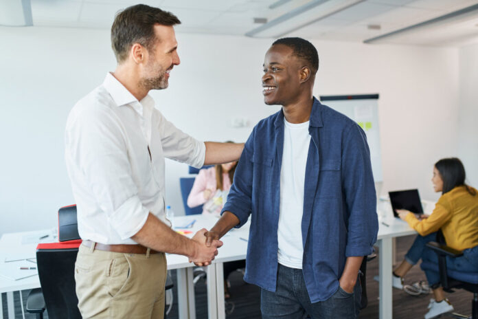 Manager begrüßt Person of Colour mit Handschlag als neuen Mitarbeiter