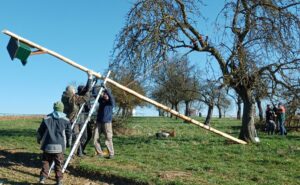 Bild: Mit vereinten Kräften montieren sechs Mitglieder der NABU-Ortsgruppe Holzheim/Dorf-Güll/Grüningen einen neuen Turmfalkenkasten in Holzheim auf einem Baumstück „Auf dem Hundshübel“ neben der Straße nach Langgöns